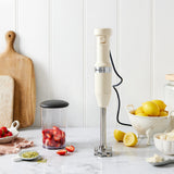 KitchenAid Corded Hand Blender Almond Cream - Hand held blender on a countertop with fruits and utensils.