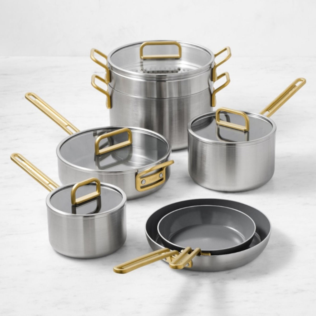 GreenPan Stanley Tucci Stainless Steel Cookware Set 6 Piece with gold handles, glass lids, and non-stick frying pans on marble surface