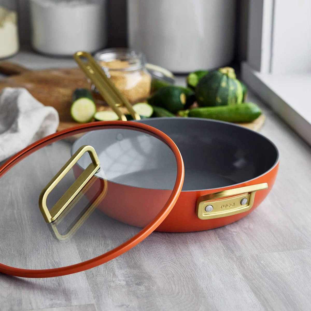 GreenPan Stanley Tucci Pan Junior Orange – angled view with glass lid resting nearby
