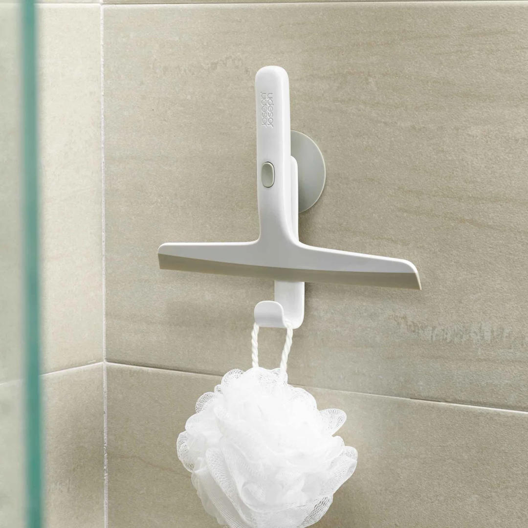 Squeegee stored neatly on wall hook with shower loofah hanging below