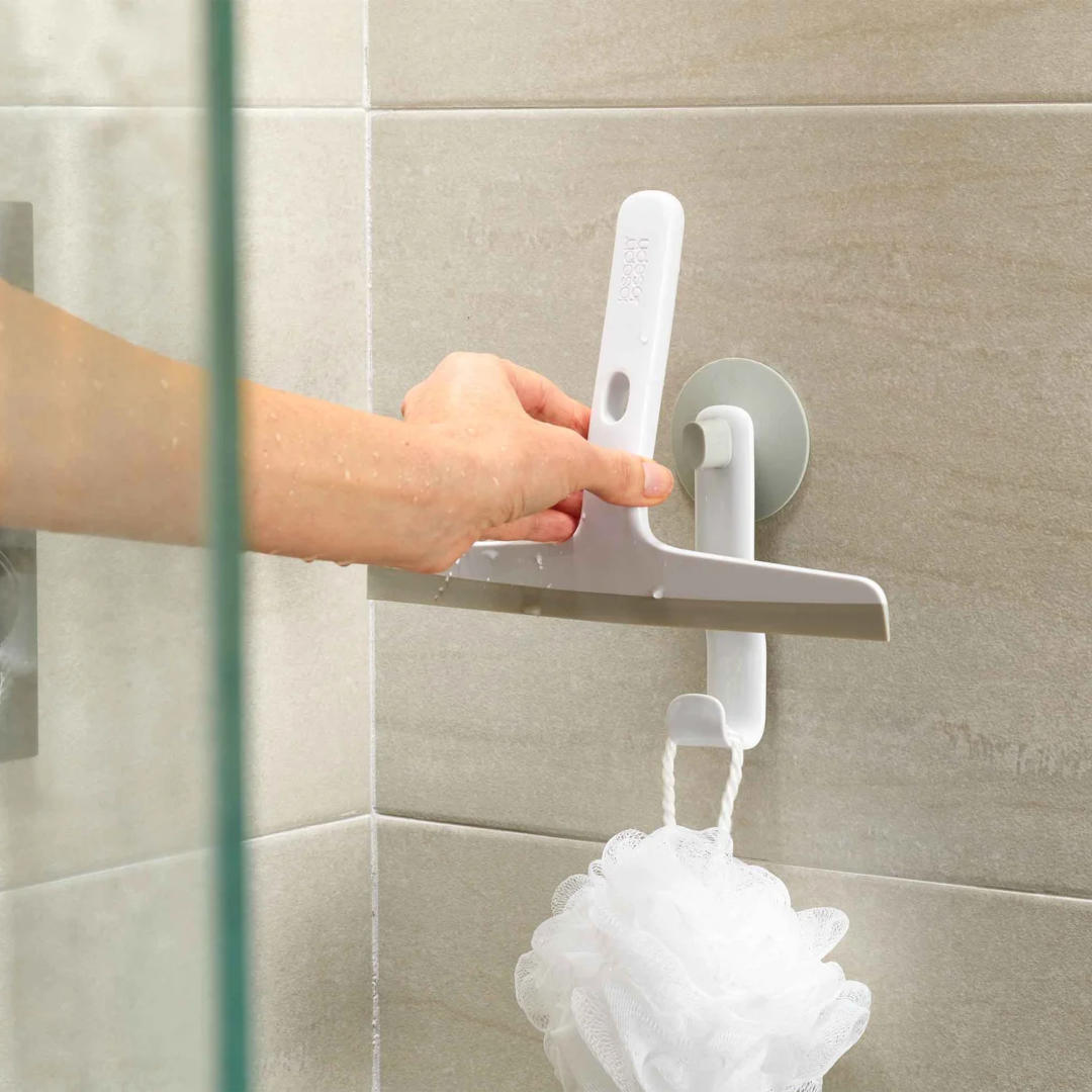 Hand placing squeegee onto wall-mounted hook in tiled shower