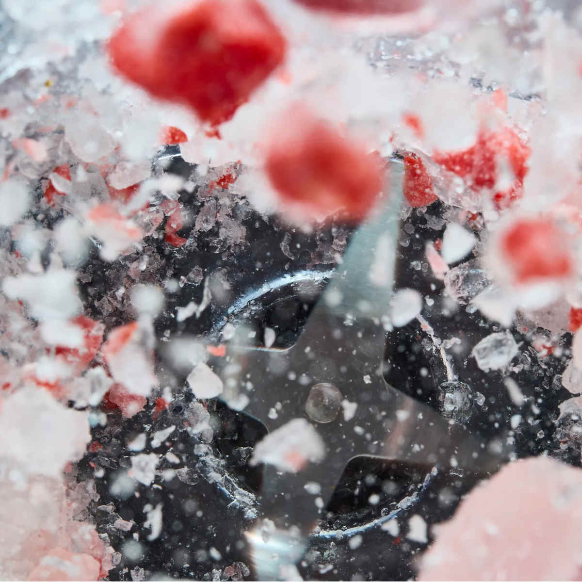 Close-up of the KitchenAid Pure Power Blender stainless steel blade crushing ice and frozen strawberries.