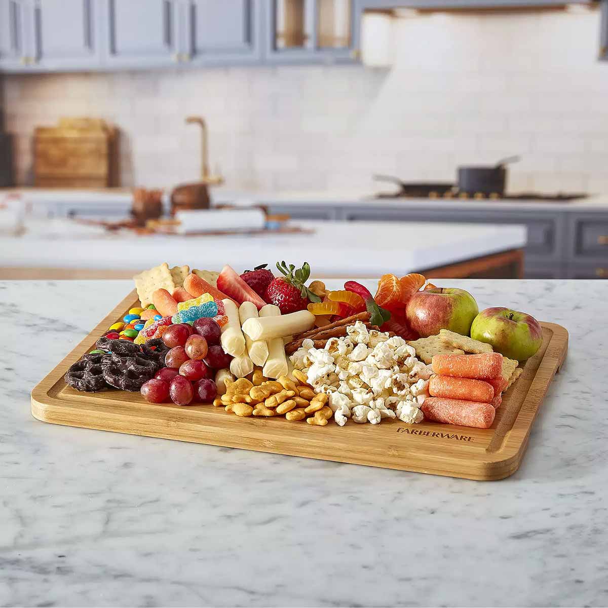 Farberware SnackleBox with Bamboo Board 30 x 40cm - Wooden charcuterie board with fruits, nuts, and cheeses on a kitchen counter.