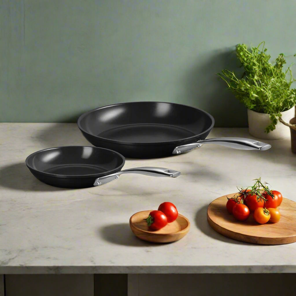 Le Creuset Essential Ceramic Non-Stick Shallow Frying Pan Set (24cm & 28cm) - Two black frying pans with silver handles on a kitchen bench