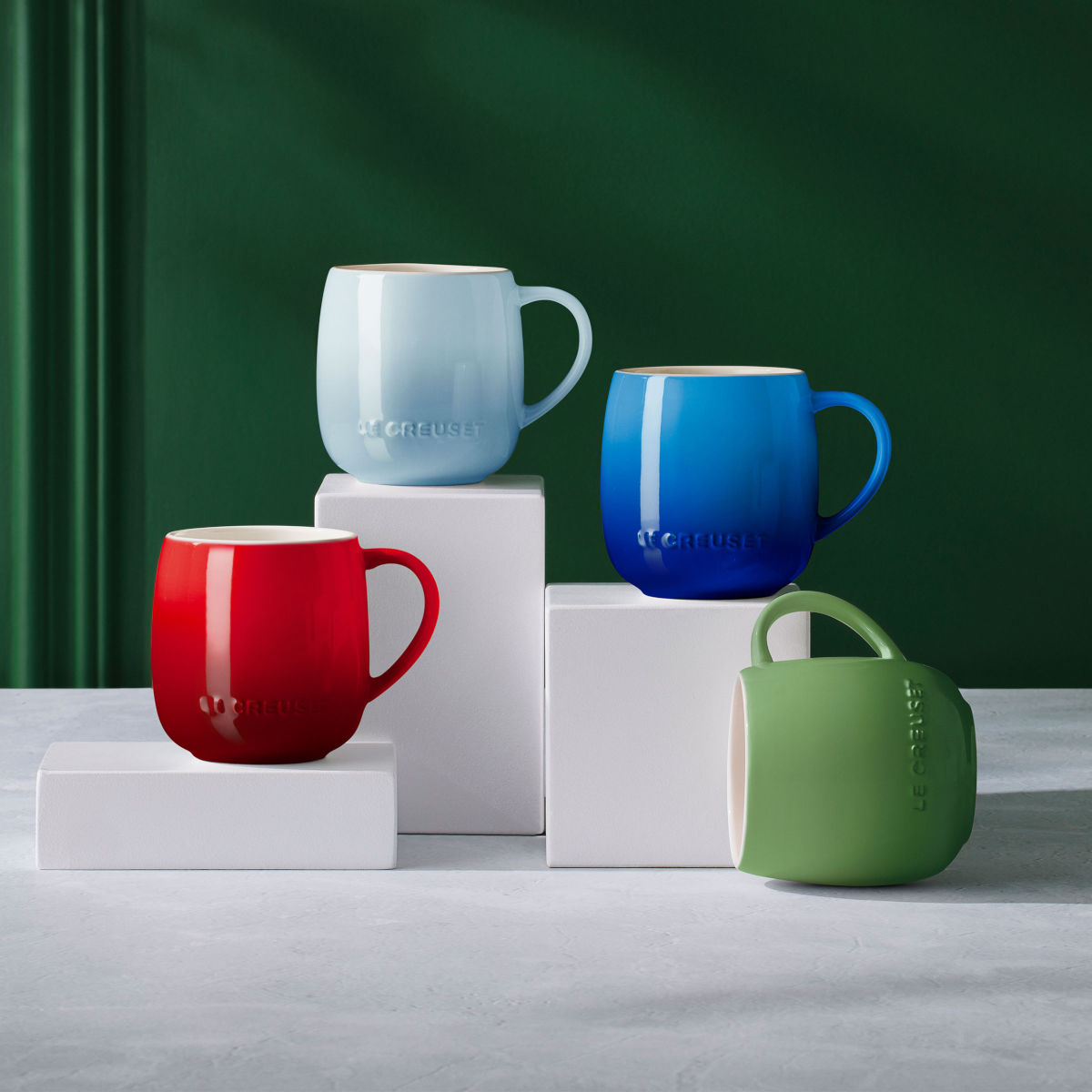 Le Creuset U Mug Coastal Blue styled with red, blue, and green mugs on white blocks