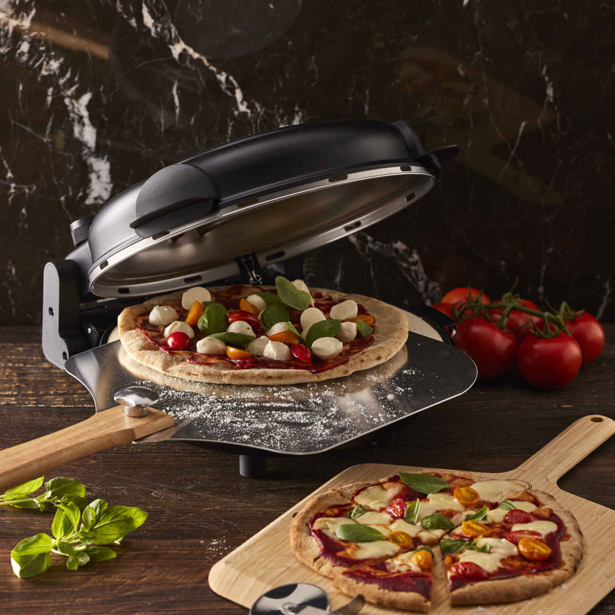 MasterPro Ultimate Pizza Oven Black open with pizza on peel, tomatoes and basil on table