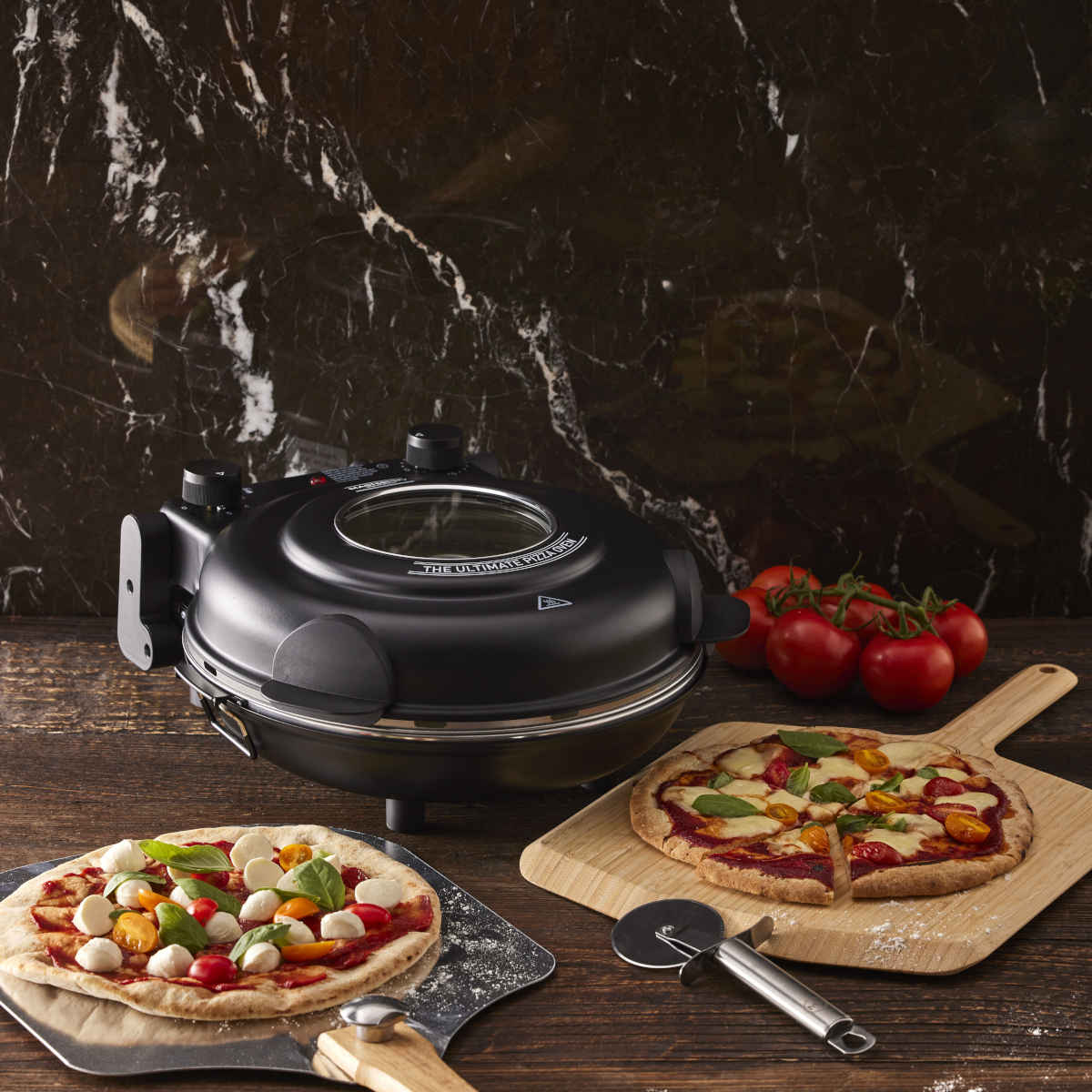 Lifestyle photo of MasterPro Ultimate Pizza Oven Black with cooked pizzas on wooden table