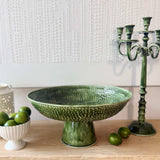 Mediterranean Market Wash Enamel Footed Tray Green 47cm, lifestyle shot on wooden table with limes and green candle holder against textured wall
