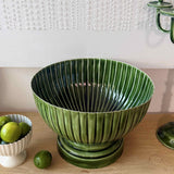 Mediterranean Market Wash Enamel Rib Vessel Green 38cm, lifestyle shot on wooden table with limes and textured wall background