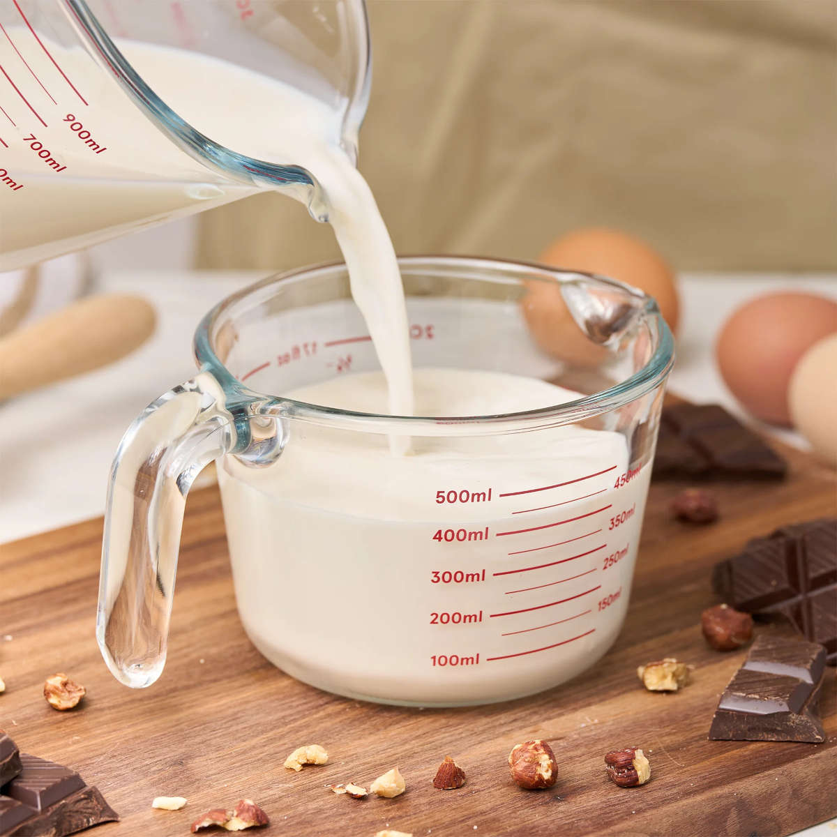 Pyrolux Measuring Jug 2 Cup (500ml) – filled with milk being poured, placed on wooden board with chocolate and eggs around